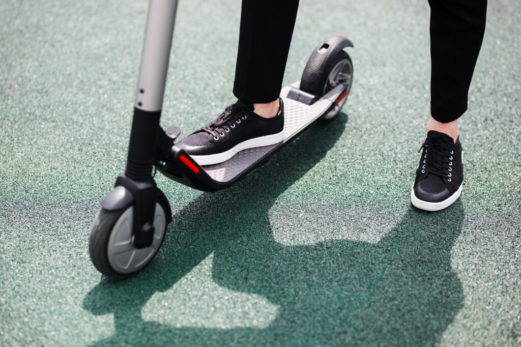 Legs of a man in stylish outfit stand on electric scooter on the street