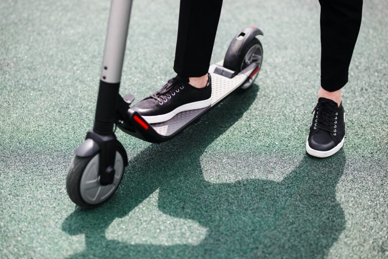 Legs of a man in stylish outfit stand on electric scooter on the street